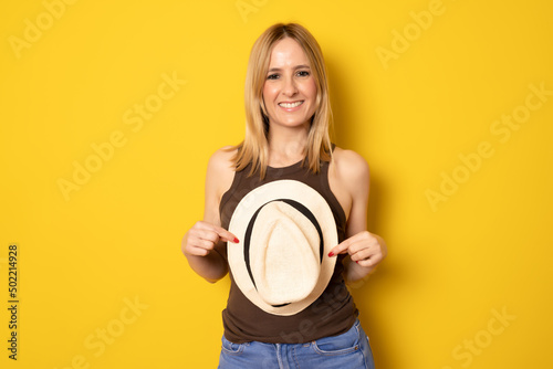 Portrait of excited smiling young woman holding straw summer hat in hands, copy space isolated on yellow background. People sincere emotions, lifestyle concept. Advertising area