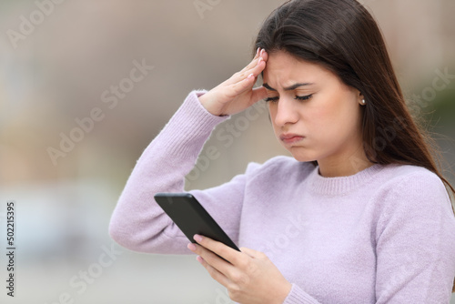Frustrated teen checking smart phone in the street photo