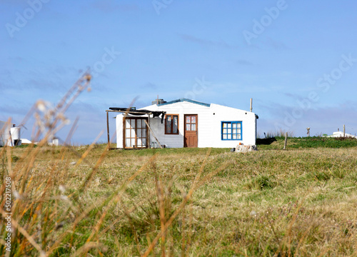 Simple house, white construction in Uruguay, grass, department of Cabo Polonio. Coastal city, coastline, beach. Housing in desert space, sparsely inhabited. Undergrowth, sunny day. Paradise view. © Pattern_Repeat