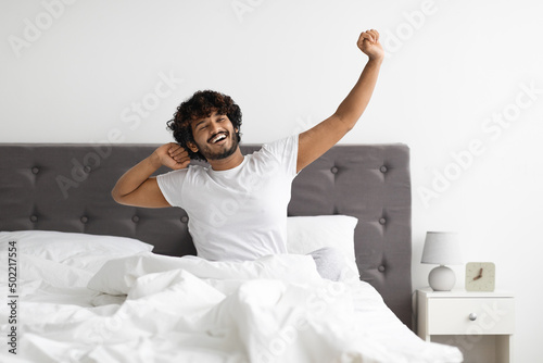 Well-rested indian guy in pajamas stretching in bed photo