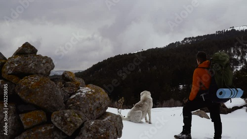 man on trekking with his dog watching the view on the mountain in winter
