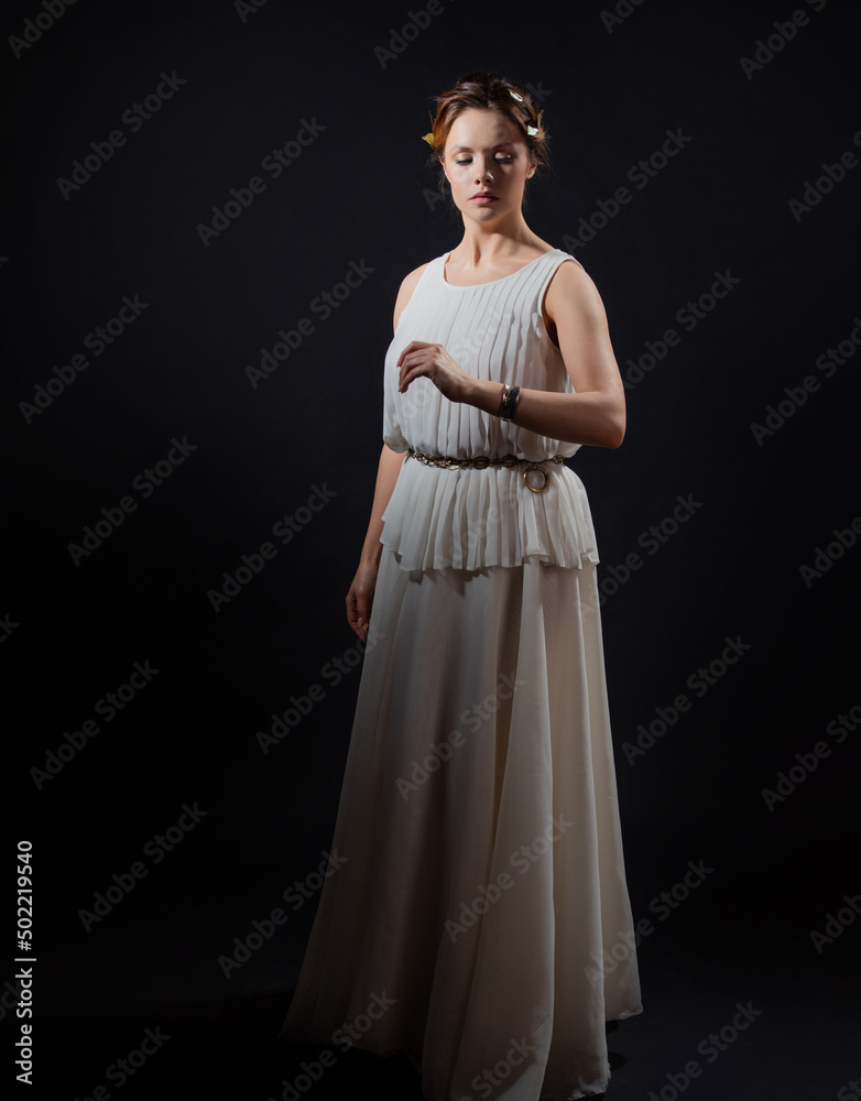 An ancient heroine, a young woman in the image of an ancient Greek goddess or muse. A noble heroine in a white tunic and a laurel wreath, a full-length photo on a black background An ancient heroine, a young woman in the image of an ancient Greek goddess or muse. A noble heroine in a white tunic and a laurel wreath, a full-length photo on a black background