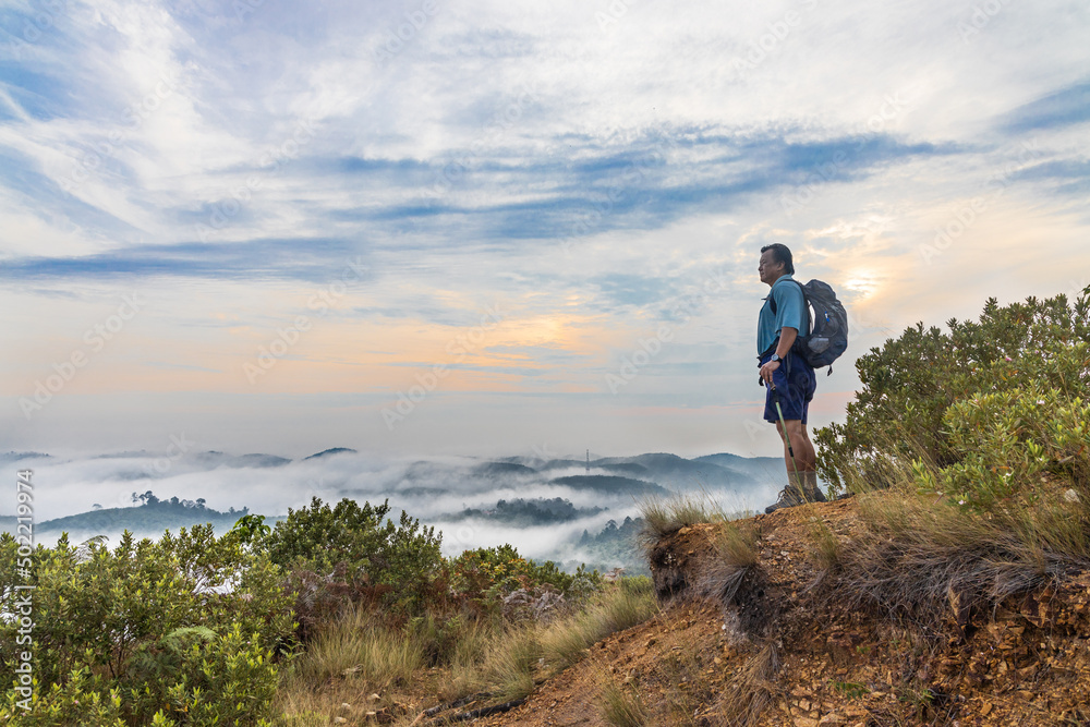 Hiker Asian man standing on peak of mountain admiring cloud scape and sunrise