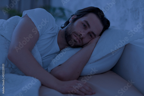 Photo Depressed man cant sleep at night, laying in bed alone