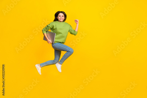 Full length photo of young girl active jumper rush hold laptop isolated over yellow color background