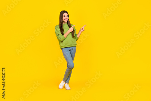 Full body photo of young cheerful girl indicate fingers empty space promo select banner isolated over yellow color background