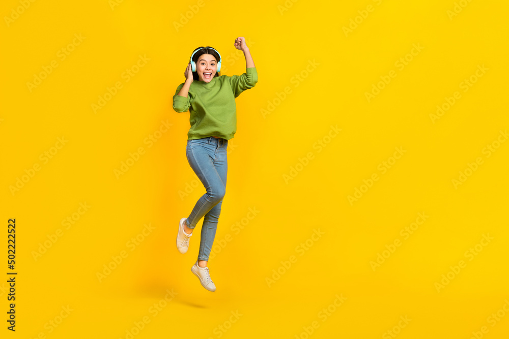 Full length photo of young active girl celebrate luck success triumph jump up listen radio isolated over yellow color background