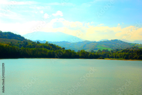 Beautiful San Ruffino lake surrounded by hills covered with green trees under the blue sky with some clouds during a sunny autumn day