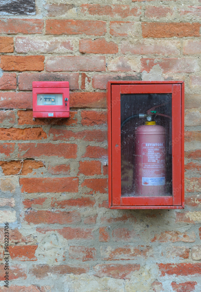 Feueralarm und Feuerlöscher in einem Kasten an einer verwitterten Wand