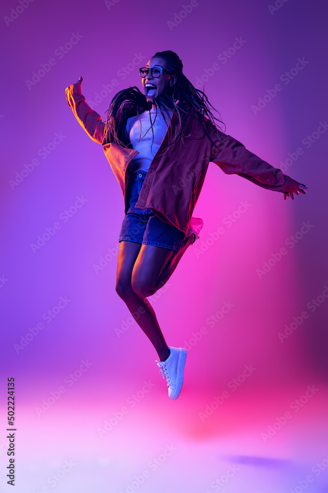 Studio shot of young excited woman in casual style outfit jumping isolated on purple background. Concept of beauty, art, fashion, youth, style