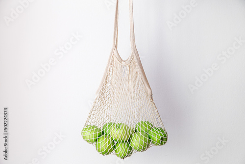 White string bag with green apples on a white background.