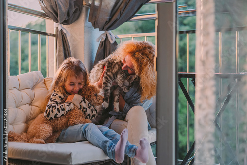 a little, happy girl, a child with a smile plays on a summer, spring vernada at home with mom and a dog at sunset. family weekend evening. Cat, dog, pets as a family member.