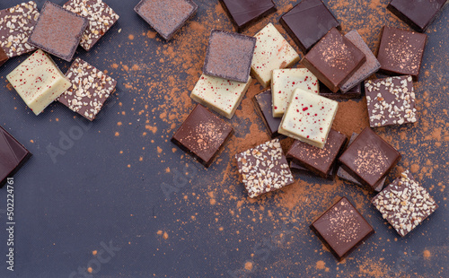Composition of bars and pieces of different milk and dark chocolate, grated cocoa on a brown background top view close up, copy space for text
