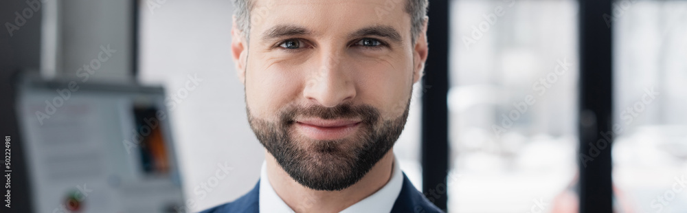 Fototapeta premium portrait of happy bearded economist smiling at camera in blurred office, banner.