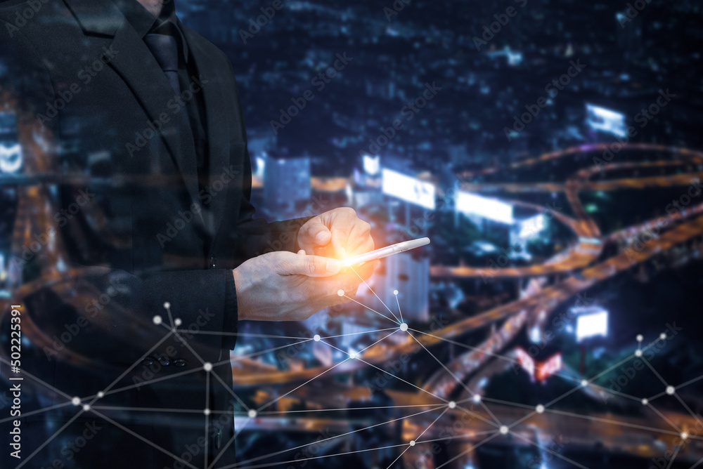 Double exposure of businessman using smartphone with blurred night cityscape, skyline and network connection. Demonstrates the use of technology to connect businesses around the world.