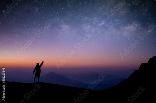 Silhouette of young traveler and backpacker standing and open arms watched the star and milky way alone on top of the mountain. He enjoyed traveling and was successful when he reached the summit.
