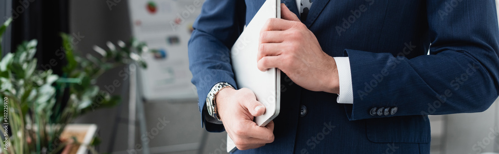 cropped view of businessman in blue blazer holding laptop in office, banner.