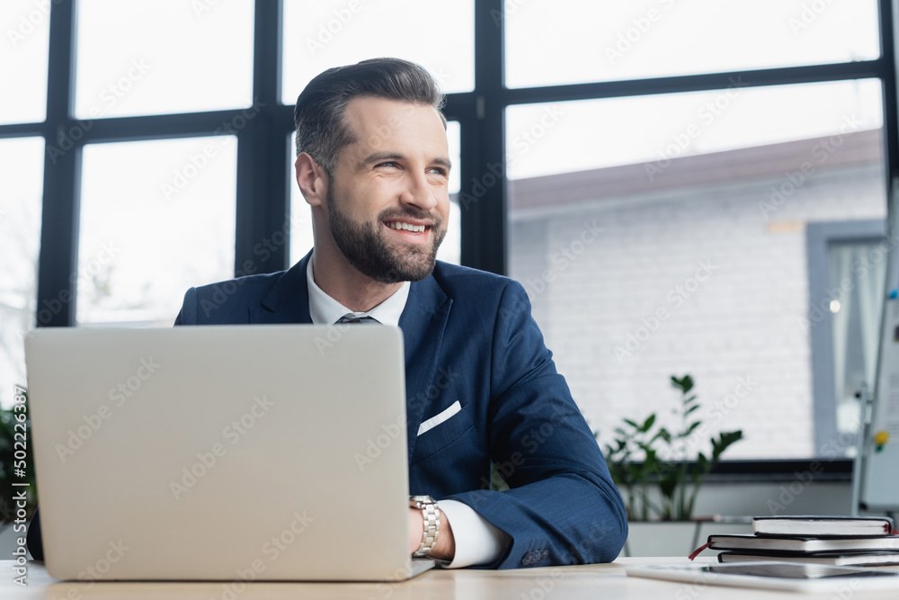 cheerful economist looking away while working near laptop and notebooks. cheerful economist looking away while working near laptop and notebooks.