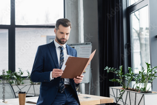 economist looking in folder while standing near desk in office.