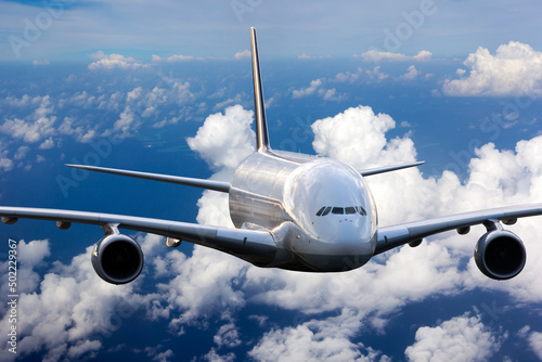 The passenger widebody plane in flight. Aircraft flies high in the blue sky above clouds. Airplane closeup front view.