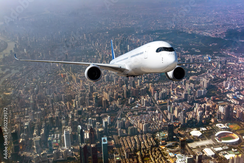 Passenger wide-body plane in flight. Aircraft flies above the skyscrapers of the business center of the big city. Front view of aircraft.