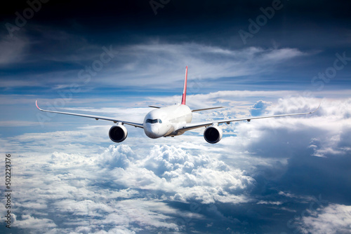 Passenger plane in flight. Aircraft flies high in the blue sky above the clouds. Front view.