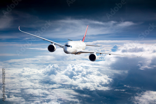 Passenger plane in flight. Aircraft flies high in the blue sky above the clouds. Front view. Right heeling.