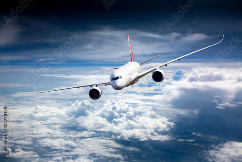Passenger plane in flight. Aircraft flies high in the blue sky above the clouds. Front view. Left heeling.