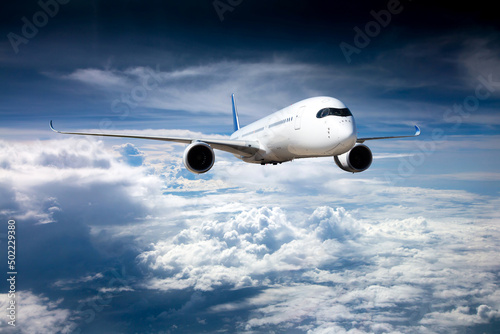 Passenger plane in flight. Aircraft flies high in the blue sky above the clouds. Front view.