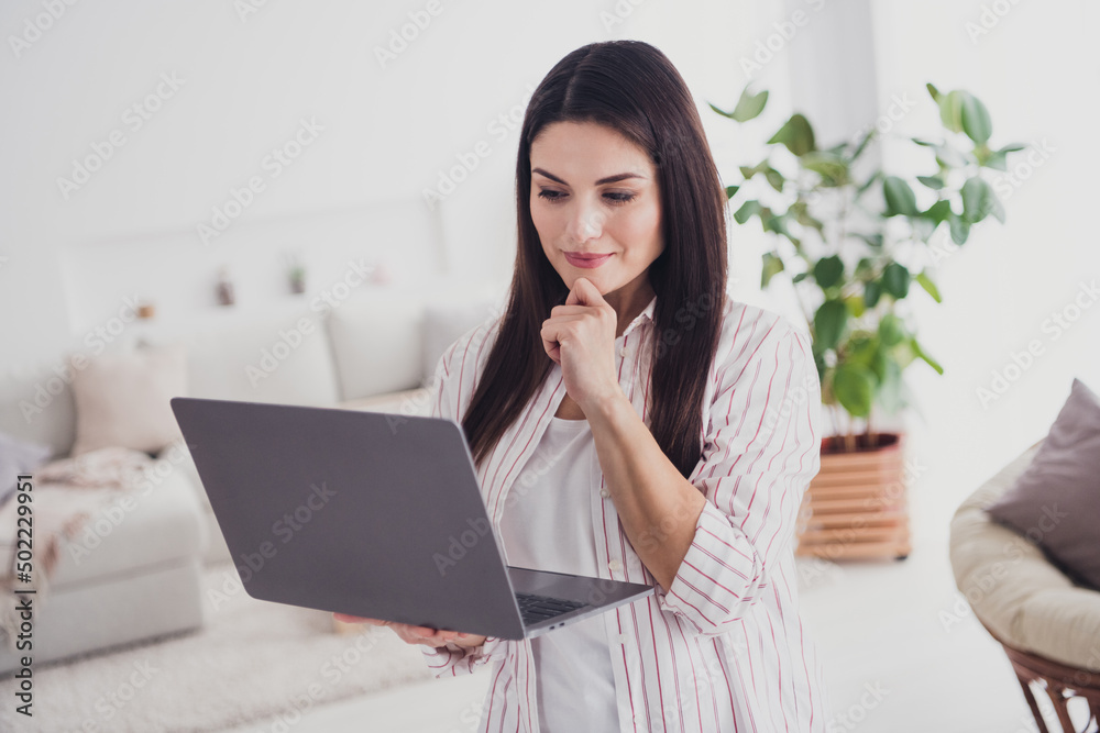 Portrait of attractive focused long-haired woman using laptop reading document presentation at home indoors Portrait of attractive focused long-haired woman using laptop reading document presentation at home indoors