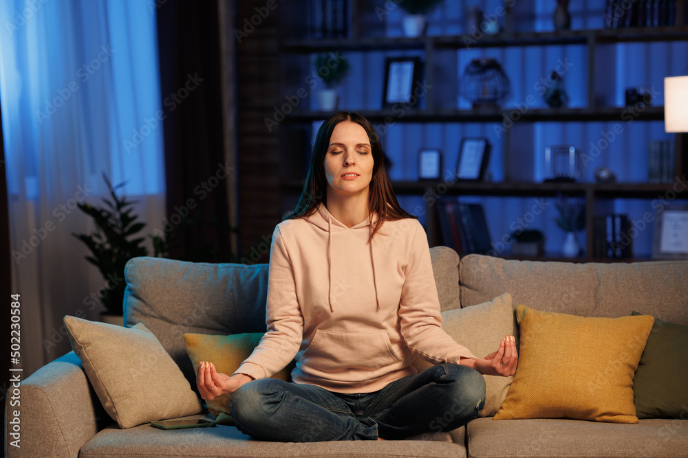Young beautiful woman with closed eyes meditates indoor, keeps hands in mudra gesture. Relaxation, leisure and stress management. Keep calm Young beautiful woman with closed eyes meditates indoor, keeps hands in mudra gesture. Relaxation, leisure and stress management. Keep calm