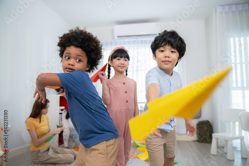Asia and African kid playing paper rocket in the kindergarten school classroom. Rocket fly in front of camera.  Learning, enjoy, education, playing concept. Feeling happing and smile during class