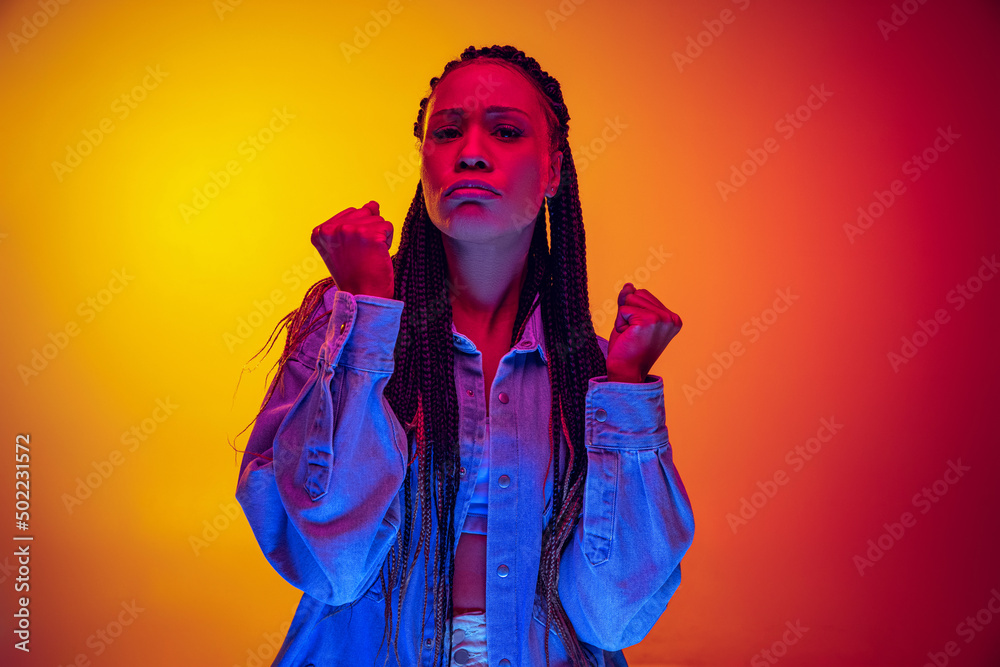 Closeup portrait of offended girl looking at camera isolated on yellow pink background in neon light. Concept of beauty, art, fashion, youth and emotions