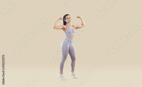 Full length studio shot of happy cheerful smiling middle aged woman wearing lilac sports bra and leggings showing her fit, strong, attractive, healthy body. Regular fitness workout at gym concept