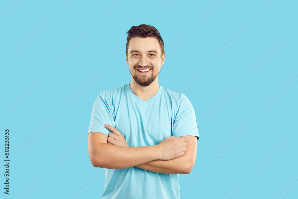 Studio shot of a happy young man in casual clothes. Portrait of a cheerful handsome guy in a blue T shirt standing with his arms crossed against a blue background, looking at the camera and smiling Studio shot of a happy young man in casual clothes. Portrait of a cheerful handsome guy in a blue T shirt standing with his arms crossed against a blue background, looking at the camera and smiling