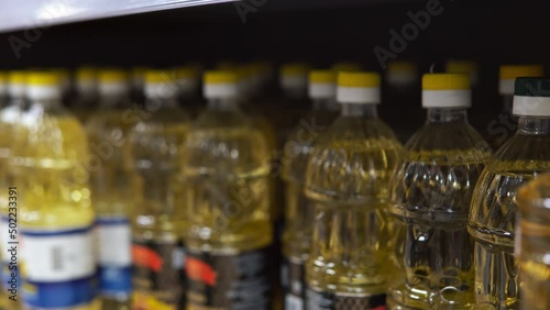 Young man alarmist buys sunflower oil in supermarket. Close up of male taking many sunflower oil bottles at grocery store. Sunflower oil shortage in Europe.
