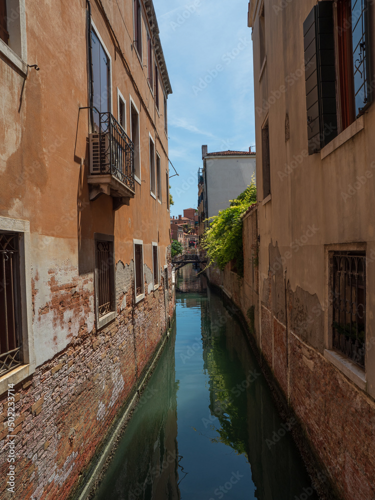 Narrow, romantic canal on a sunny day in Venice.