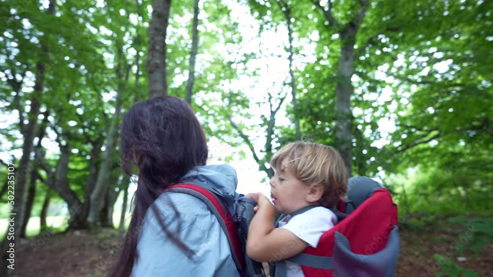 Mother carrying son in backpack carrier mom hiking with child in nature Mother carrying son in backpack carrier mom hiking with child in nature