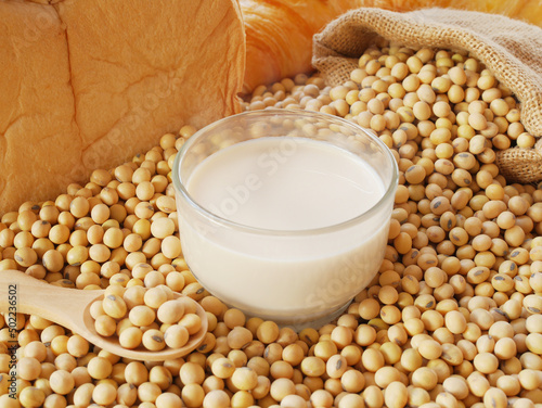 A glass soy milk on some soy beans with sack of soy beans and spoon of soy beans and some breads and some croissant