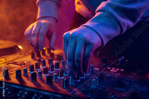 Close-up image in neon lights. Male hands turning sounds on professional dj mixer. Live performance