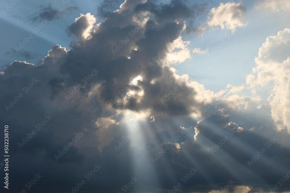 The sun's rays break through gray dense clouds at sunset. Shining light in the evening sky. Natural background.