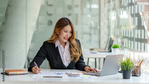 Beautiful Asian business woman sitting working on laptop computer and document in the office.