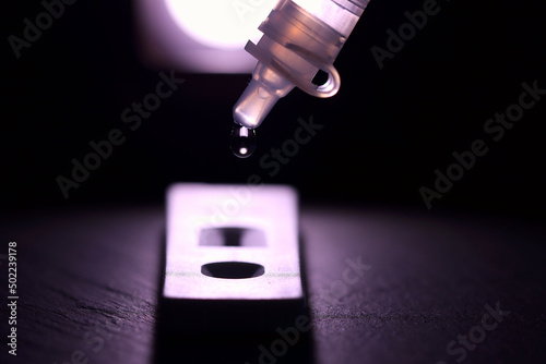 A backlit view of a dropper for a covid 19,  lateral flow test. Focus is on dropper with the generic test cassette below. Shallow depth of field. 
