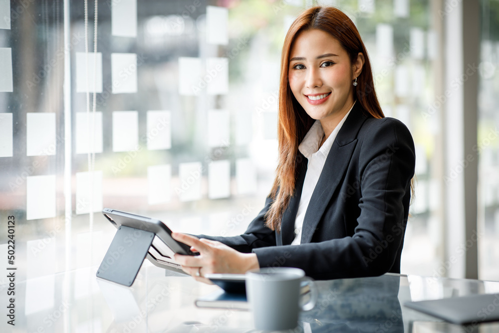 Portrait of Young Asian woman hand freelancer is working her job on computer tablet in modern office. Doing accounting analysis report real estate investment data, Financial and tax systems concept. Portrait of Young Asian woman hand freelancer is working her job on computer tablet in modern office. Doing accounting analysis report real estate investment data, Financial and tax systems concept.