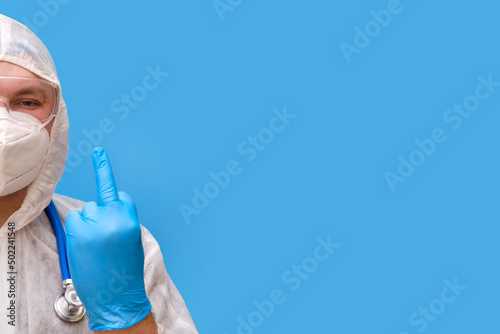 Doctor in a protective suit uniform with goggles and medical face mask on a studio blue background, copy space
