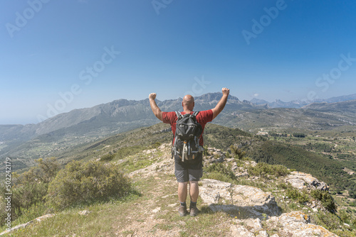 Unrecognizable man hiker with his arms raised, with a gesture of happiness and success, with mountains in the background