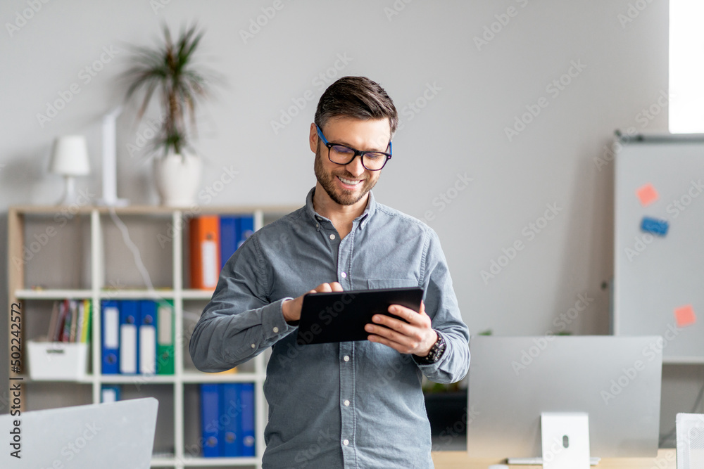 Portrait of cheerful mature businessman using computer tablet in office, looking at screen and smiling, copy space Portrait of cheerful mature businessman using computer tablet in office, looking at screen and smiling, copy space