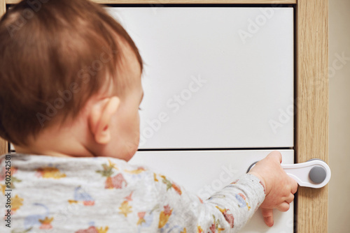 Toddler baby boy rips off a cabinet drawer with his hand. The child holds the cabinet door handle, small kid photo