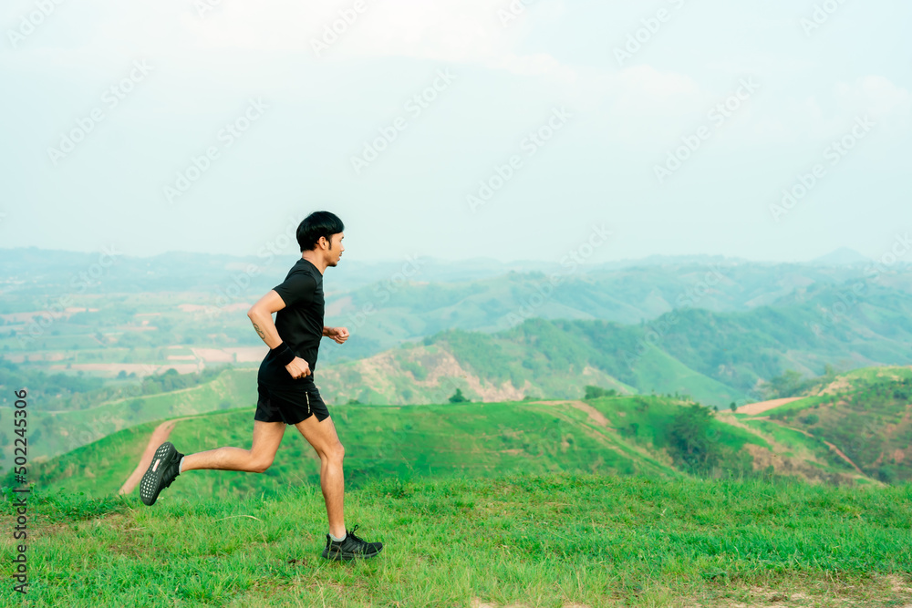 Obraz premium Portrait of an Asian male trail runner running. On the high mountains there are beautiful views. It's a trail running practice. on a bright day Behind is a beautiful mountain view.