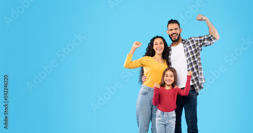Happy Arabic Family Showing Biceps Standing Over Blue Studio Background © Prostock-studio